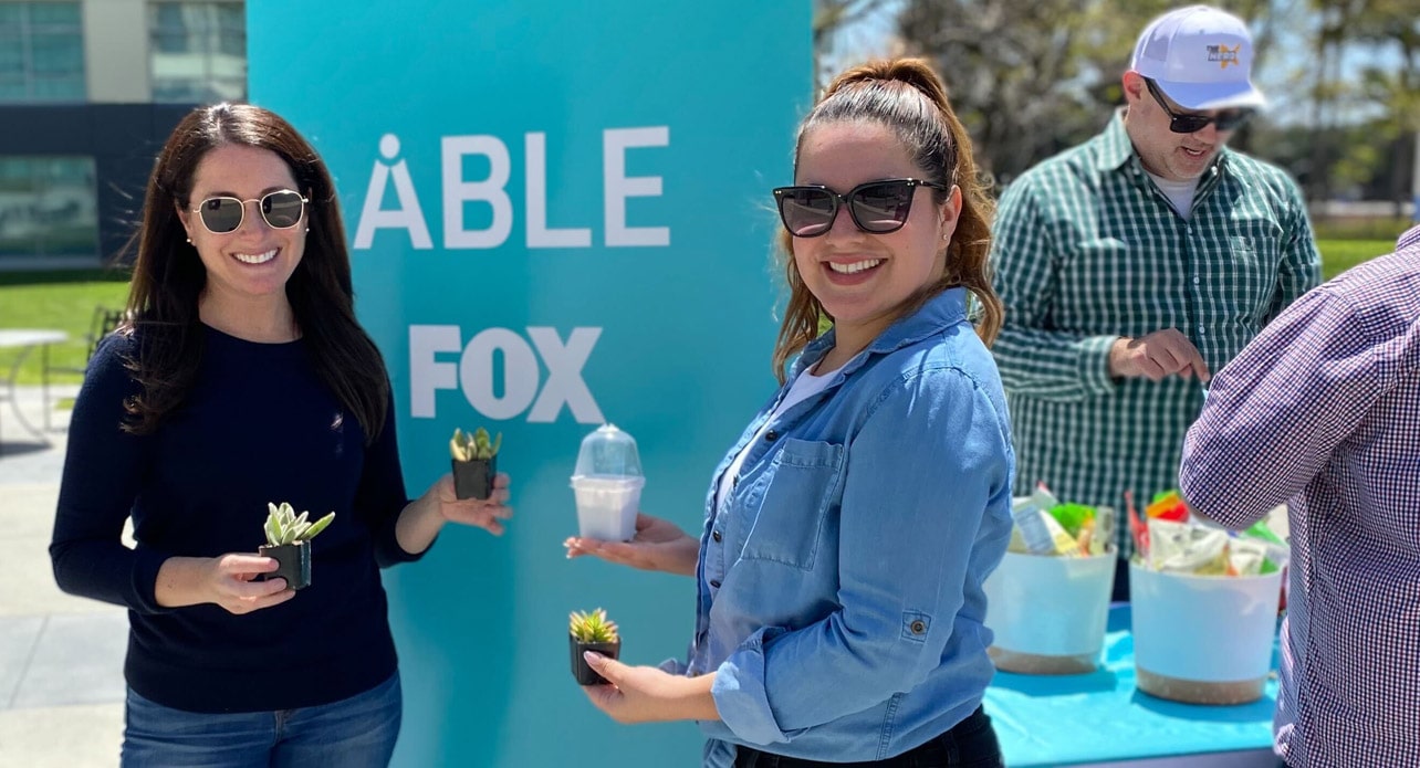 Two FOX employees standing at an ABLE event holding baby plants